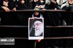 دختر نوجوان در تشییع پیکر شهیدان گمنام عکس رهبر معظم انقلاب را به دست گرفته است .