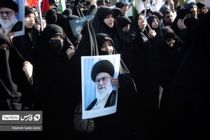 بانویی که در تشیع پیکر شهیدان گمنام عکس رهبر معظم انقلاب را در دست دارد مشغول سوگواری است.