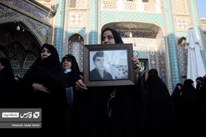 یکی از بانوان با عکس پدر شهیدش به مراسم تشییع پیکر شهیدان گمنام آمده است .