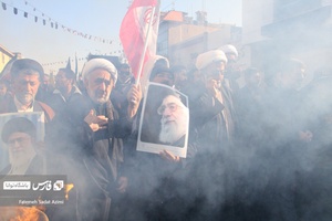 دو نفر از طلاب در تشییع شهیدان گمنام عکس رهبر معظم انقلاب را به دست گرفته اند.